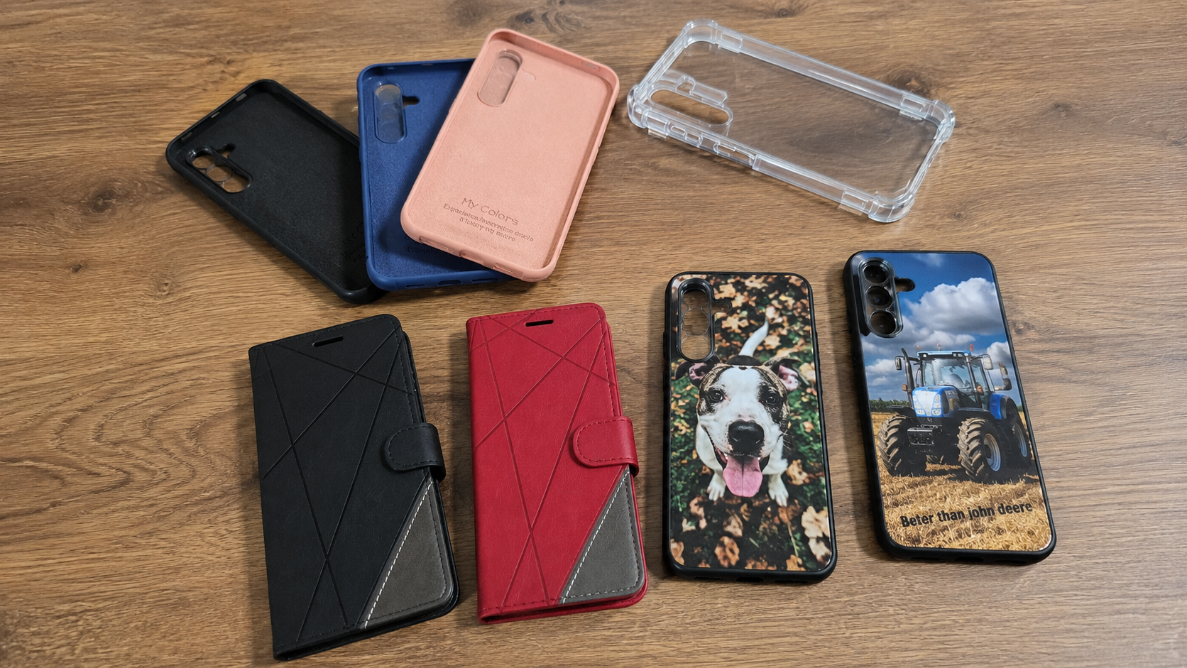 Assorted smartphone cases on a wooden table: black, blue, pink, red wallet-style with gray corner, clear bumper, plus two phones with images (dog and tractor).